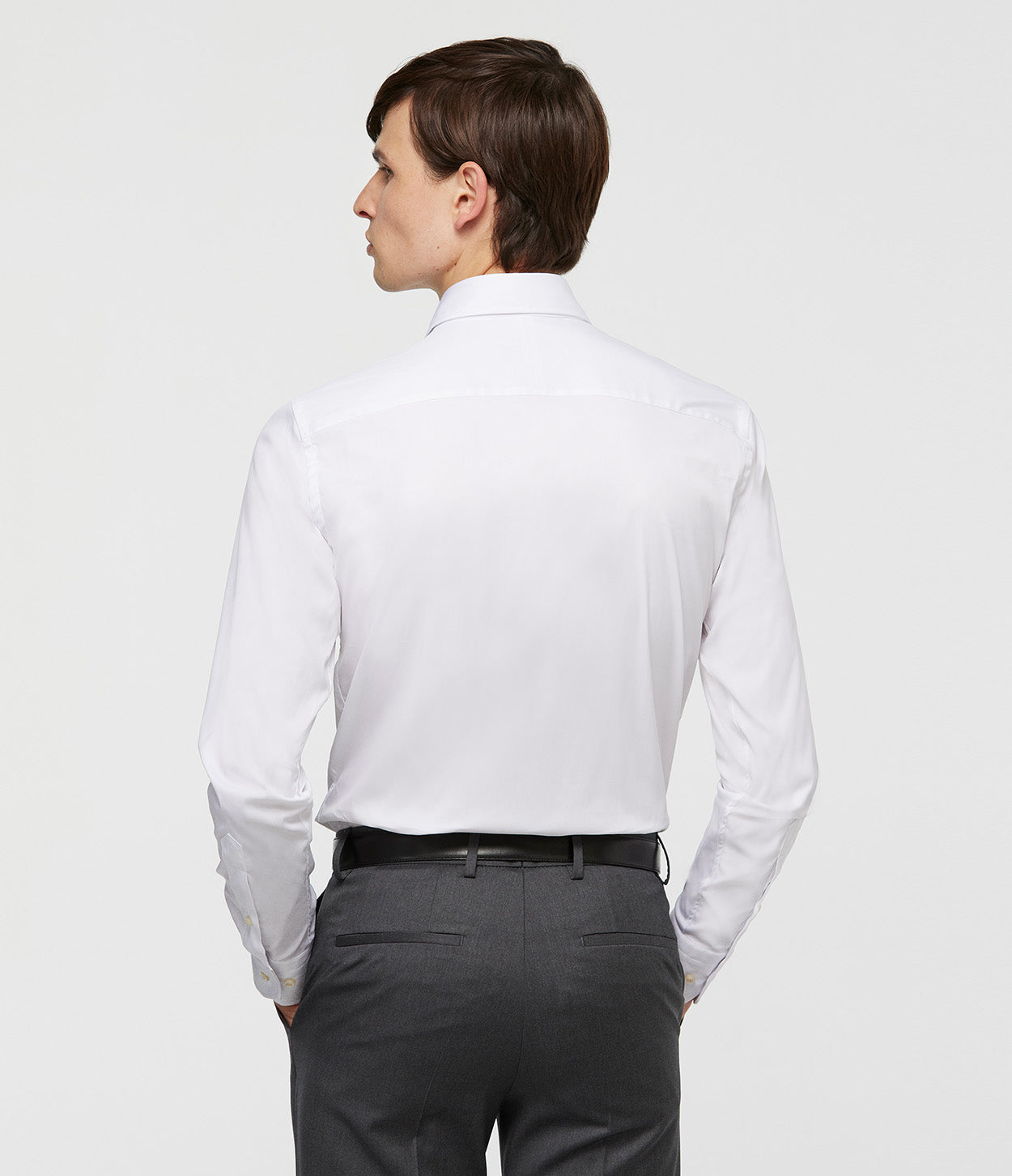 modelo de espaldas con camisa blanca manga larga y manos en los bolsillos